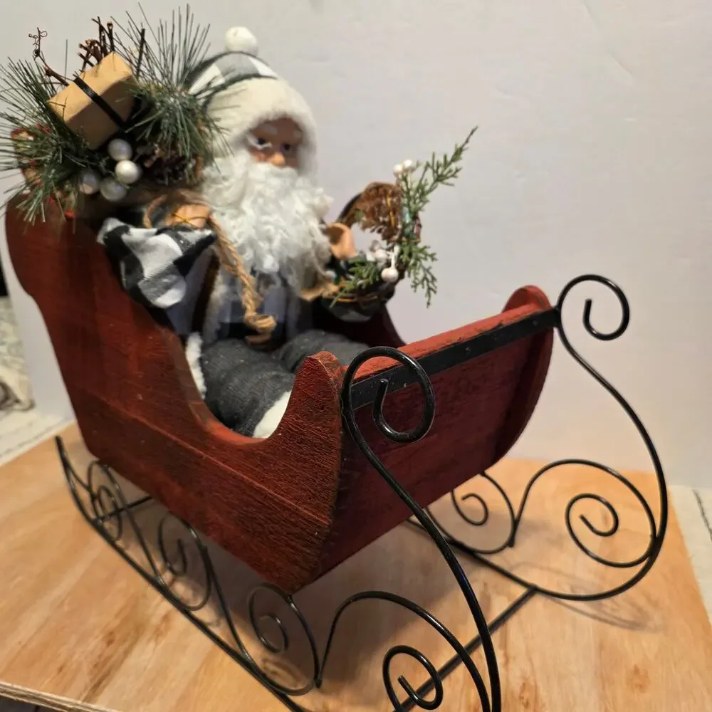 Santa dressed in black/white gingham riding in a red wooden sleigh w/presents